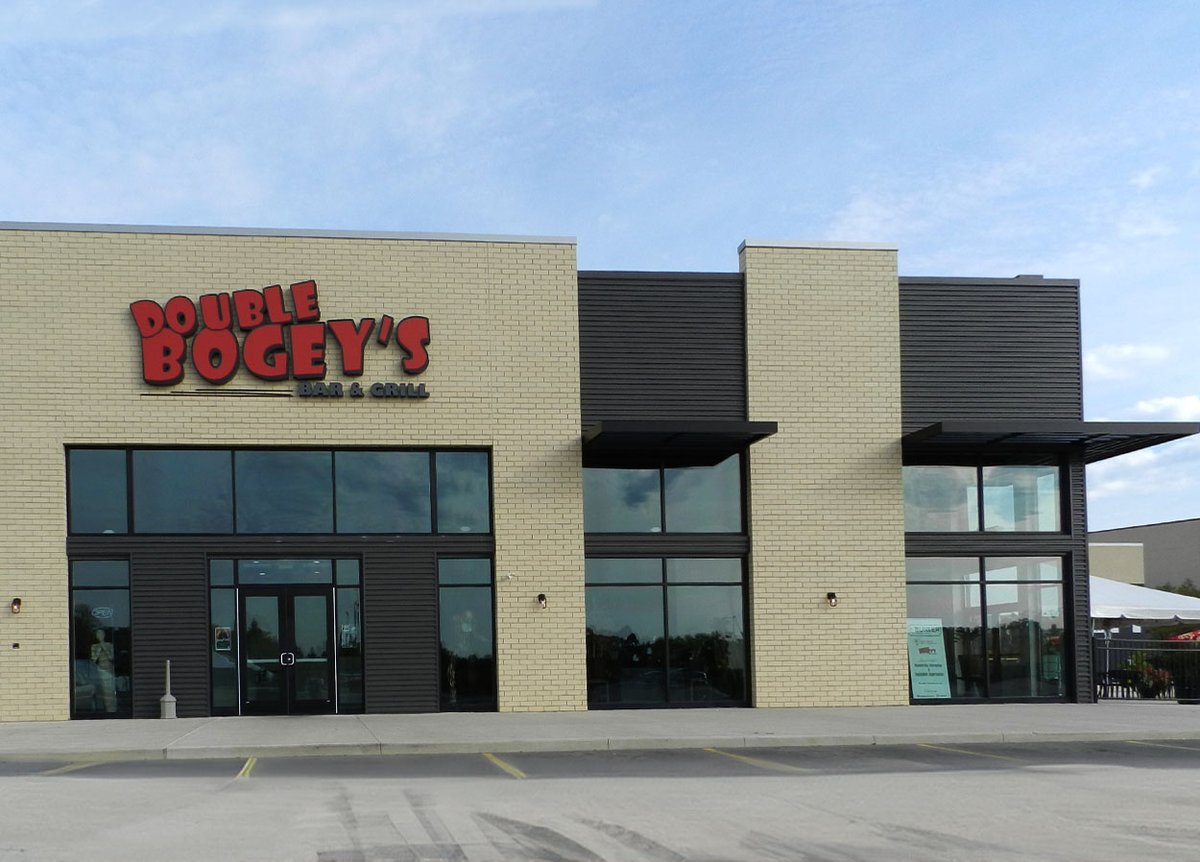 Exterior of Double Bogey's Bar & Grill. The building has a beige brick facade with a large red and black sign that reads 'Double Bogey's Bar & Grill.' The entrance features large glass windows and doors. The sky is clear and blue, and the parking lot in front of the building is empty.